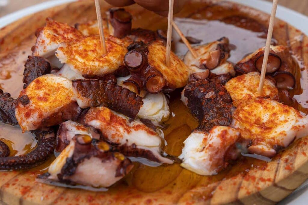 Pulpo à la Gallega appétissant sur une assiette en bois avec pommes de terre, huile d'olive et paprika.